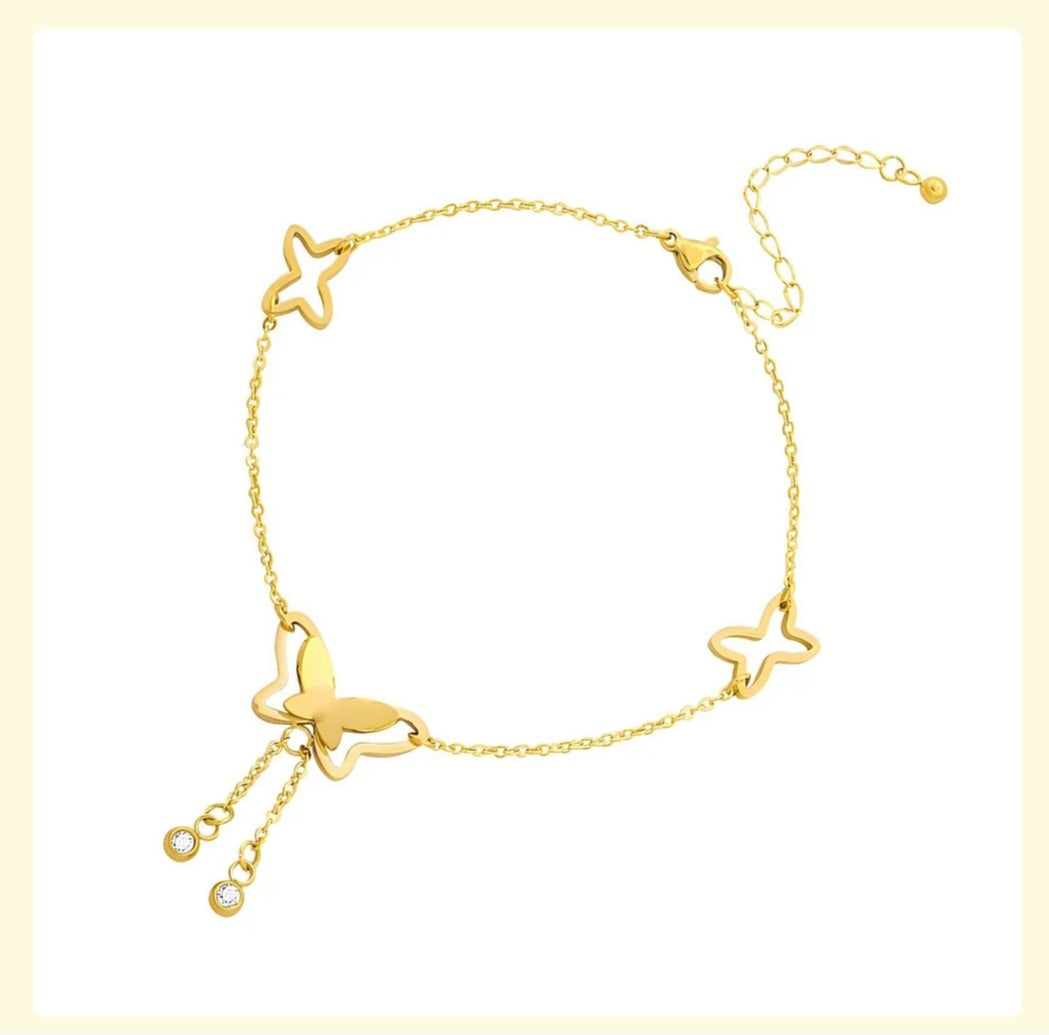 Gold anklet with butterfly and star designs on a light yellow background