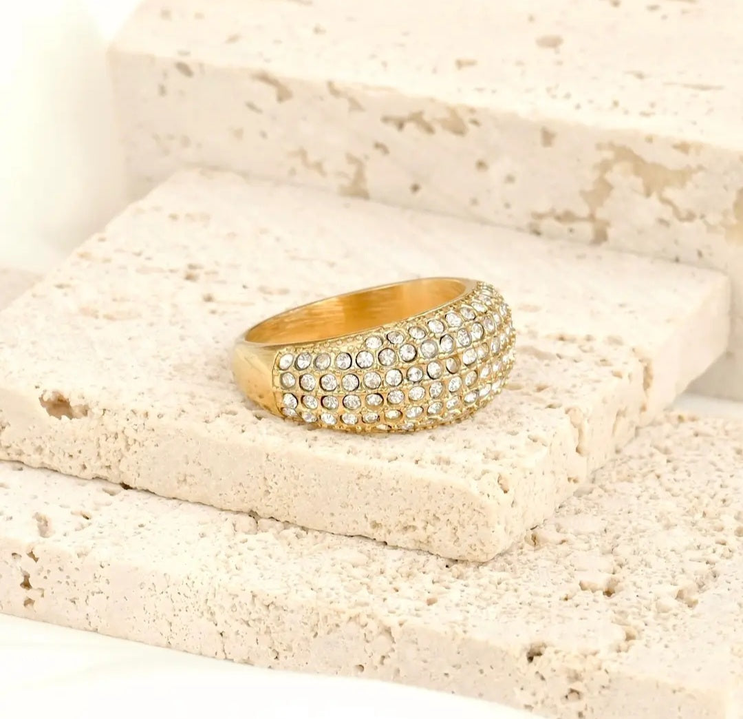 Gold ring with cubic zirconia crystals on a textured beige surface
