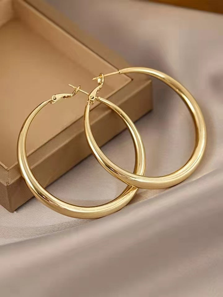 Large gold hoop earrings on a beige surface with a brown box in the background