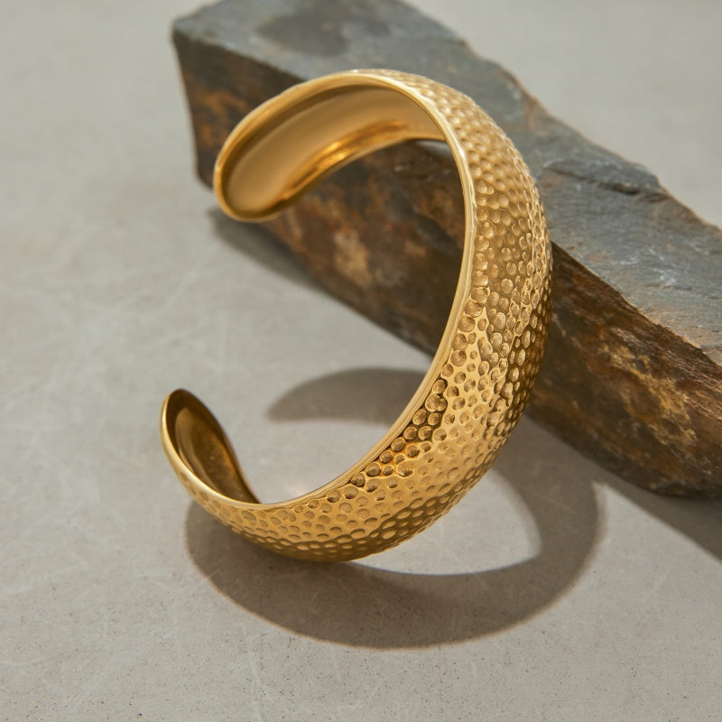Gold textured open cuff bracelet on a stone surface