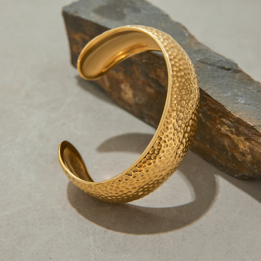 Gold textured open cuff bracelet on a stone surface