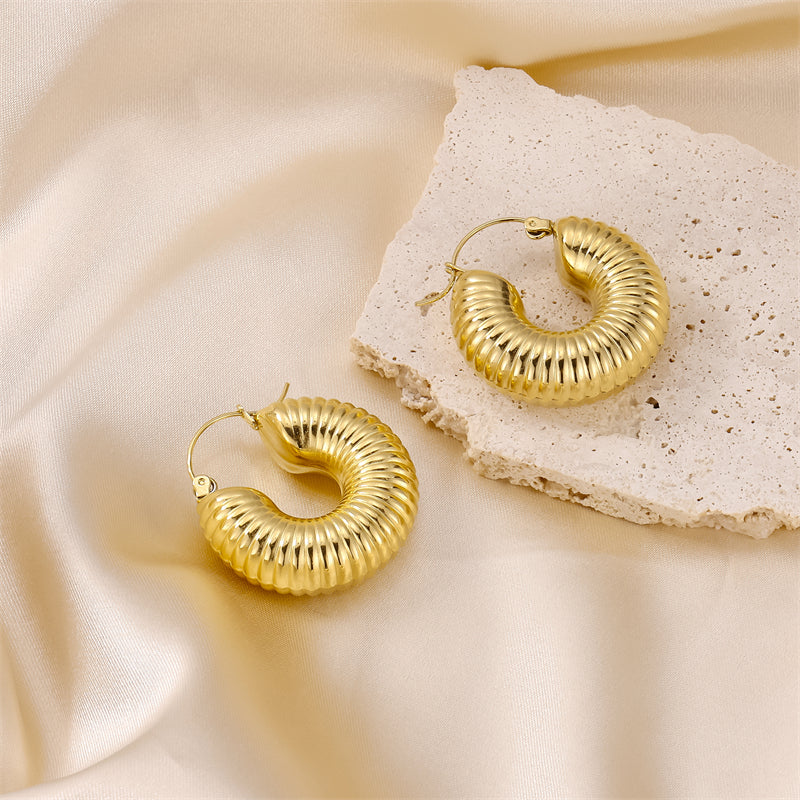 Gold ribbed textured hoop earrings on a beige surface