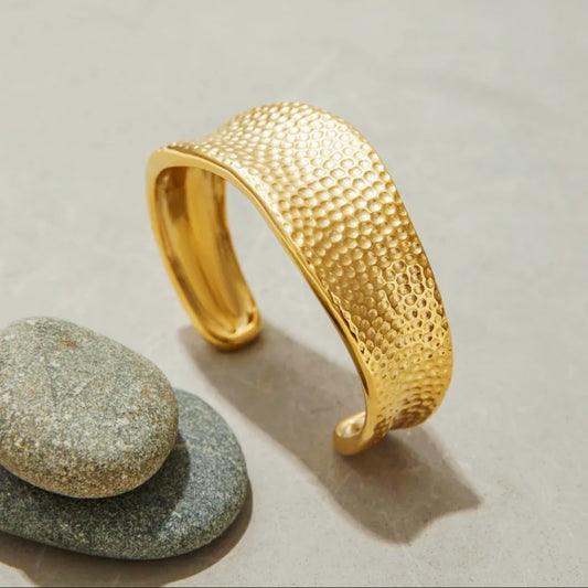 Gold textured bracelet on a light surface with stones