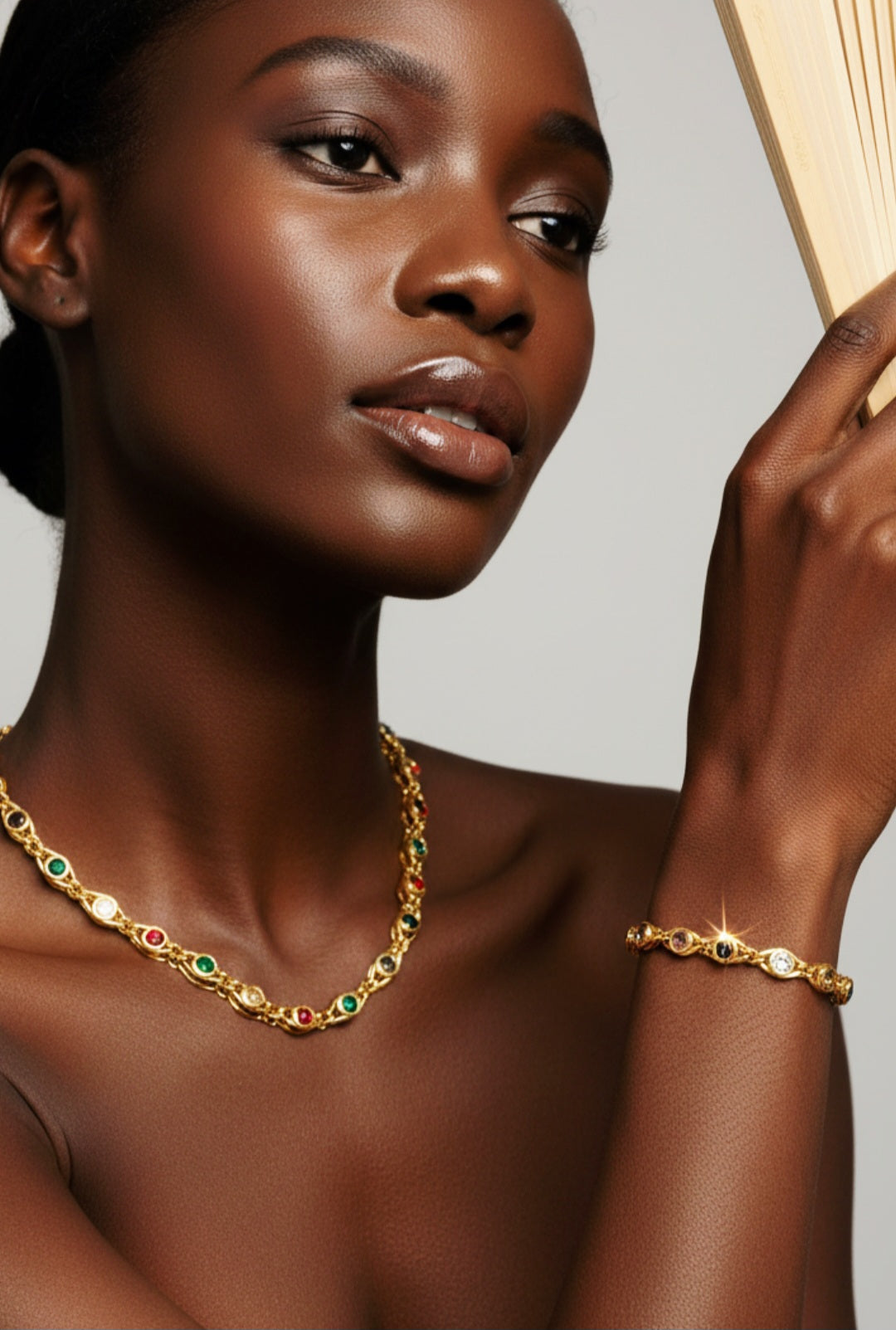 Woman wearing gold necklace and bracelet with multi-color crystals against a neutral background