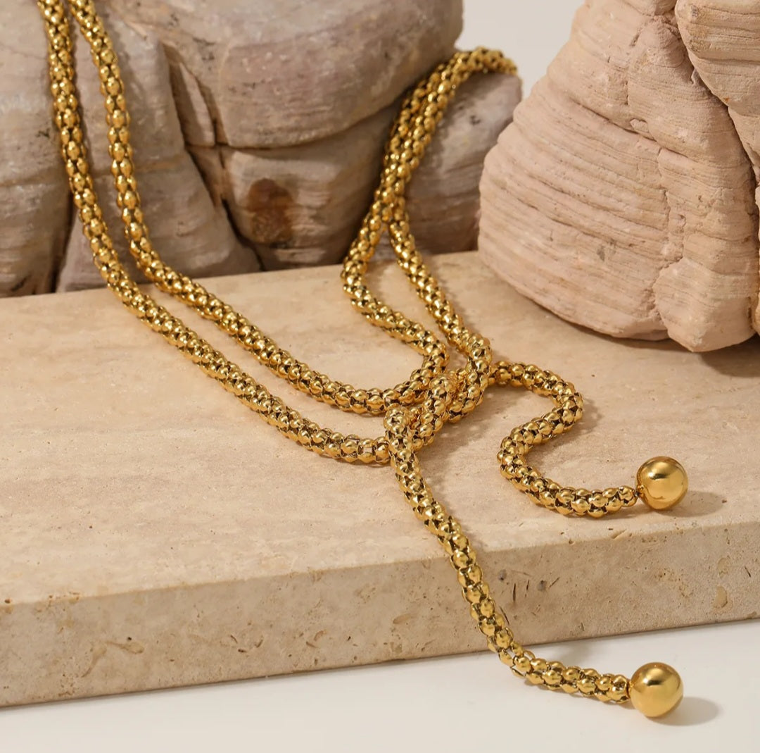 Gold necklace with spherical ends on a stone surface