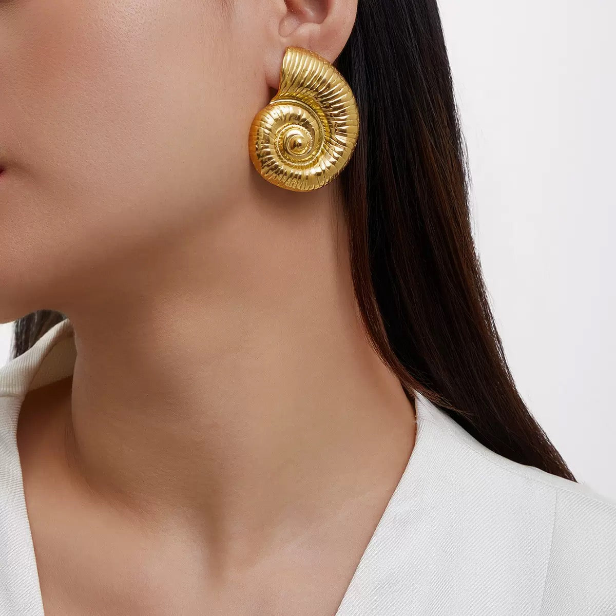 Close-up of a person wearing gold nautilus shell shaped earrings on a white background.