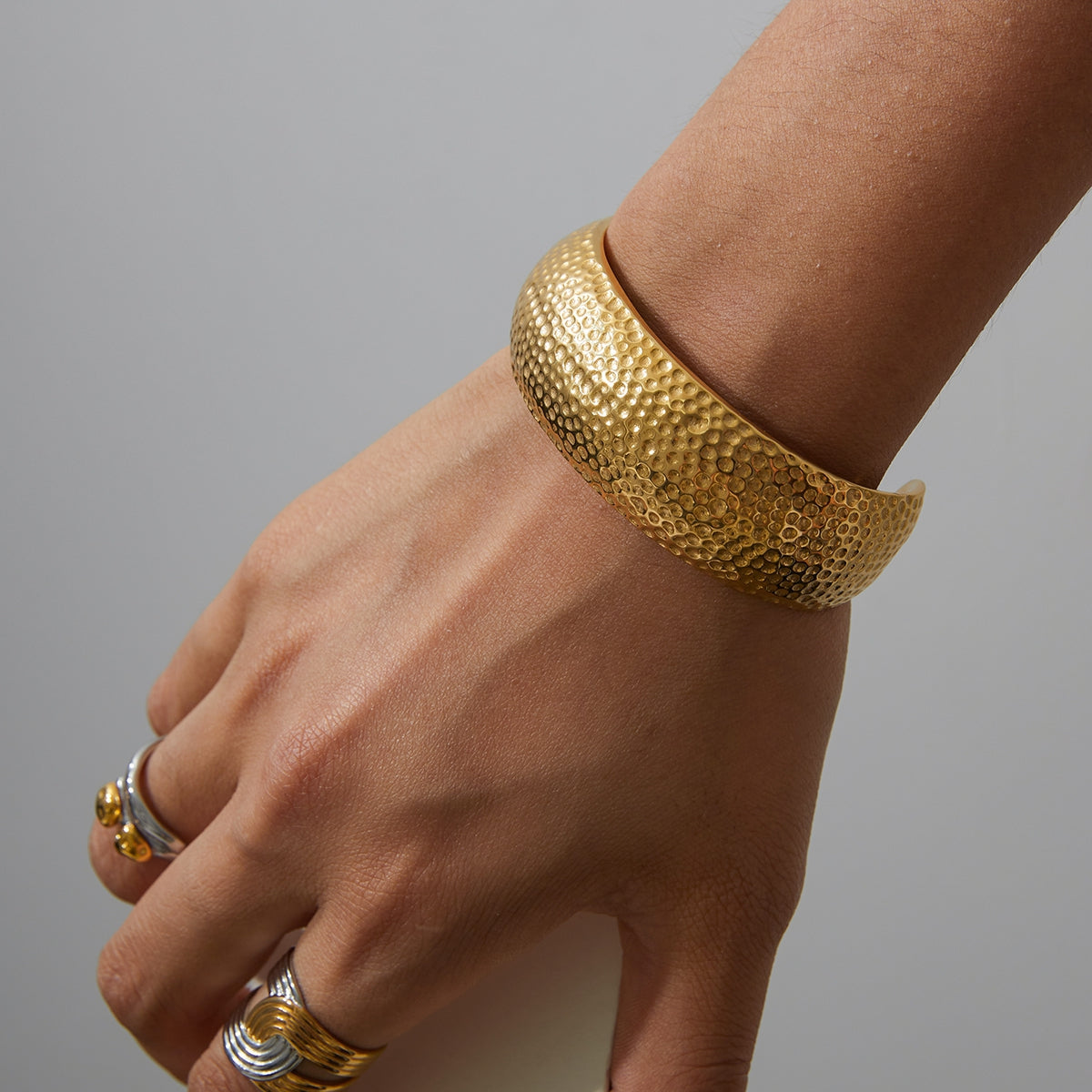 Gold textured open cuff bracelet on a wrist with a gray background