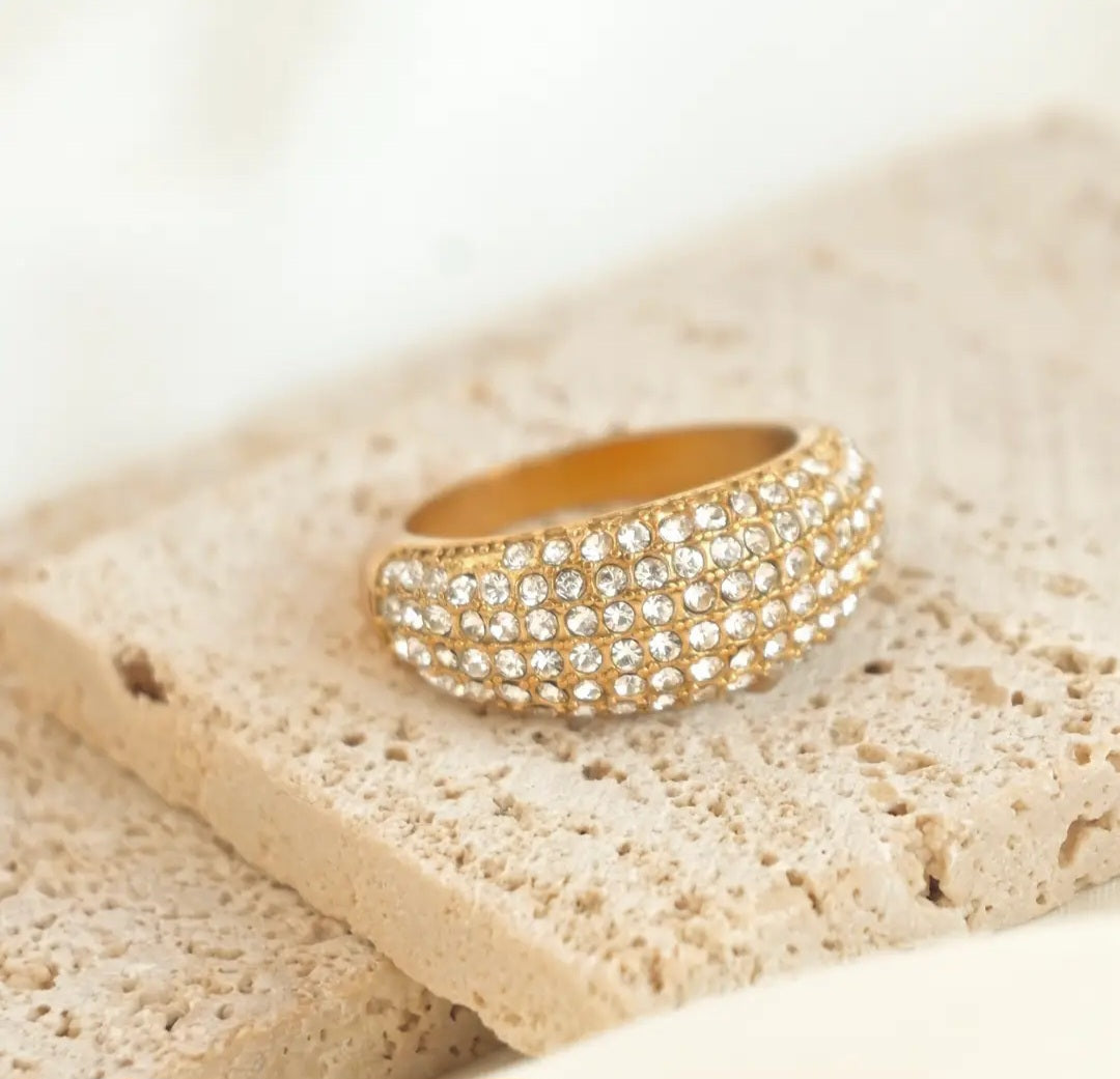 Gold dome ring with cubic zirconia crystals in pave setting on a beige stone surface