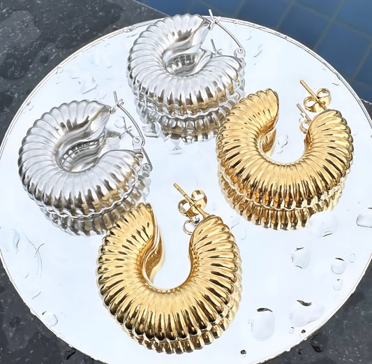 Gold and silver hoop earrings on a round metallic surface with water droplets.