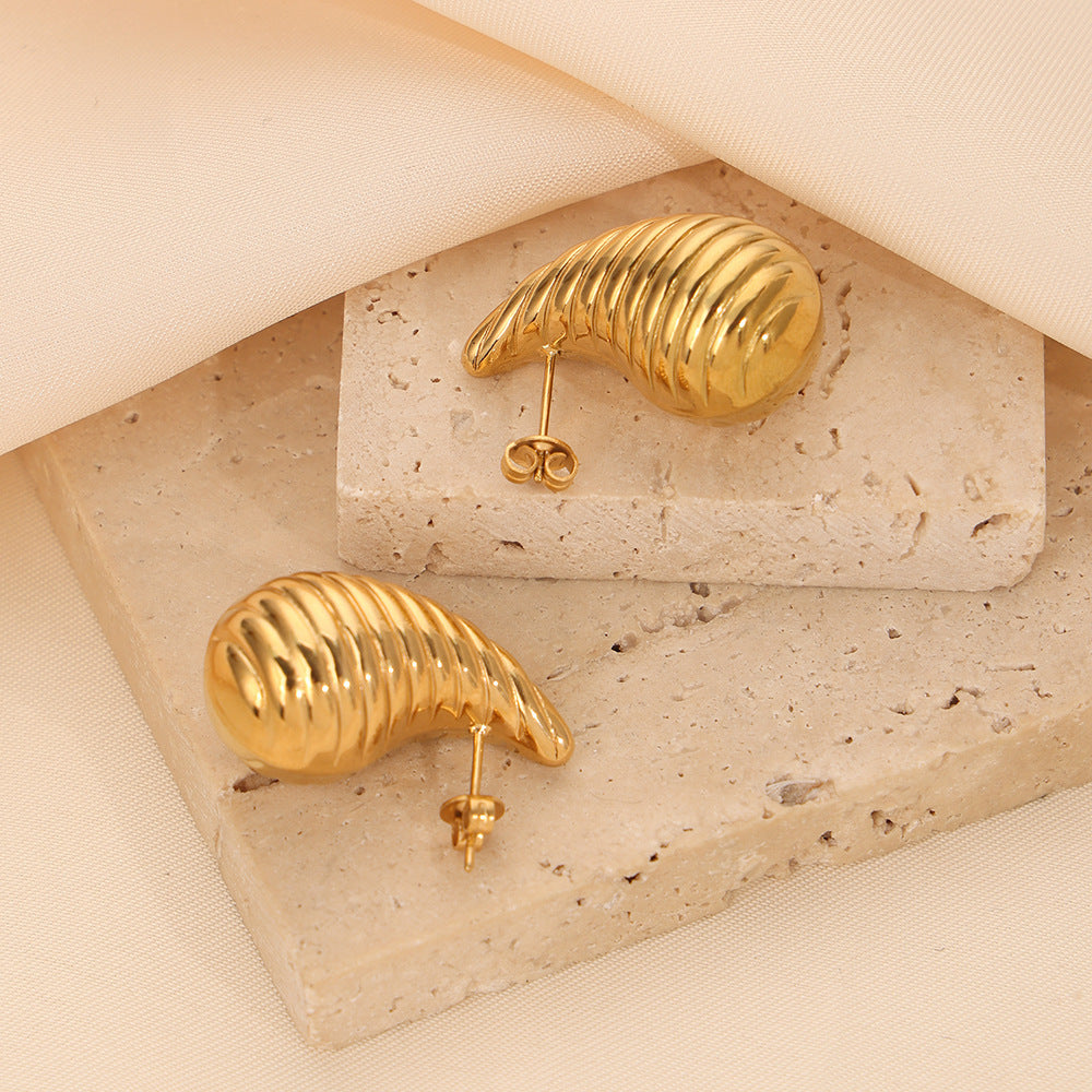 Gold teardrop shape earrings on a textured stone surface with a soft beige background