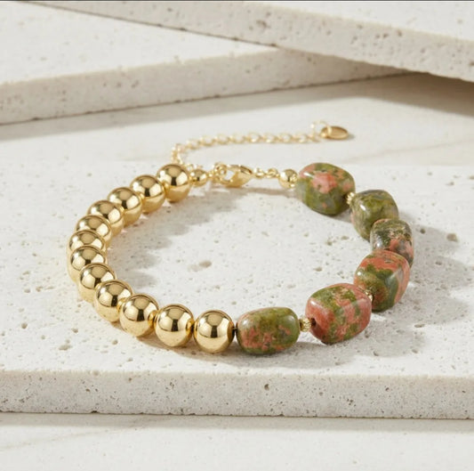 Bracelet with gold beads and green  and pink stone beads on a light surface